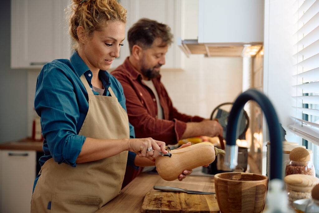 Mid adult woman peeling pumpkin while cooking Thanksgiving meal with her husband in the kitchen • Experience Hope Counseling