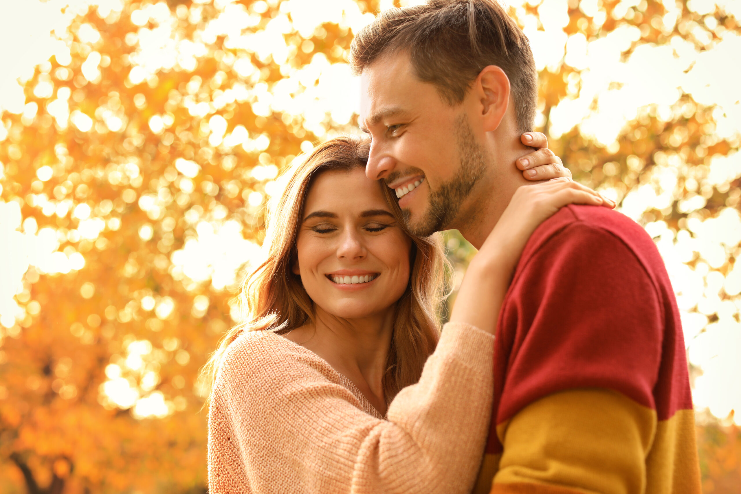 Smiling couple embracing outdoors under autumn trees