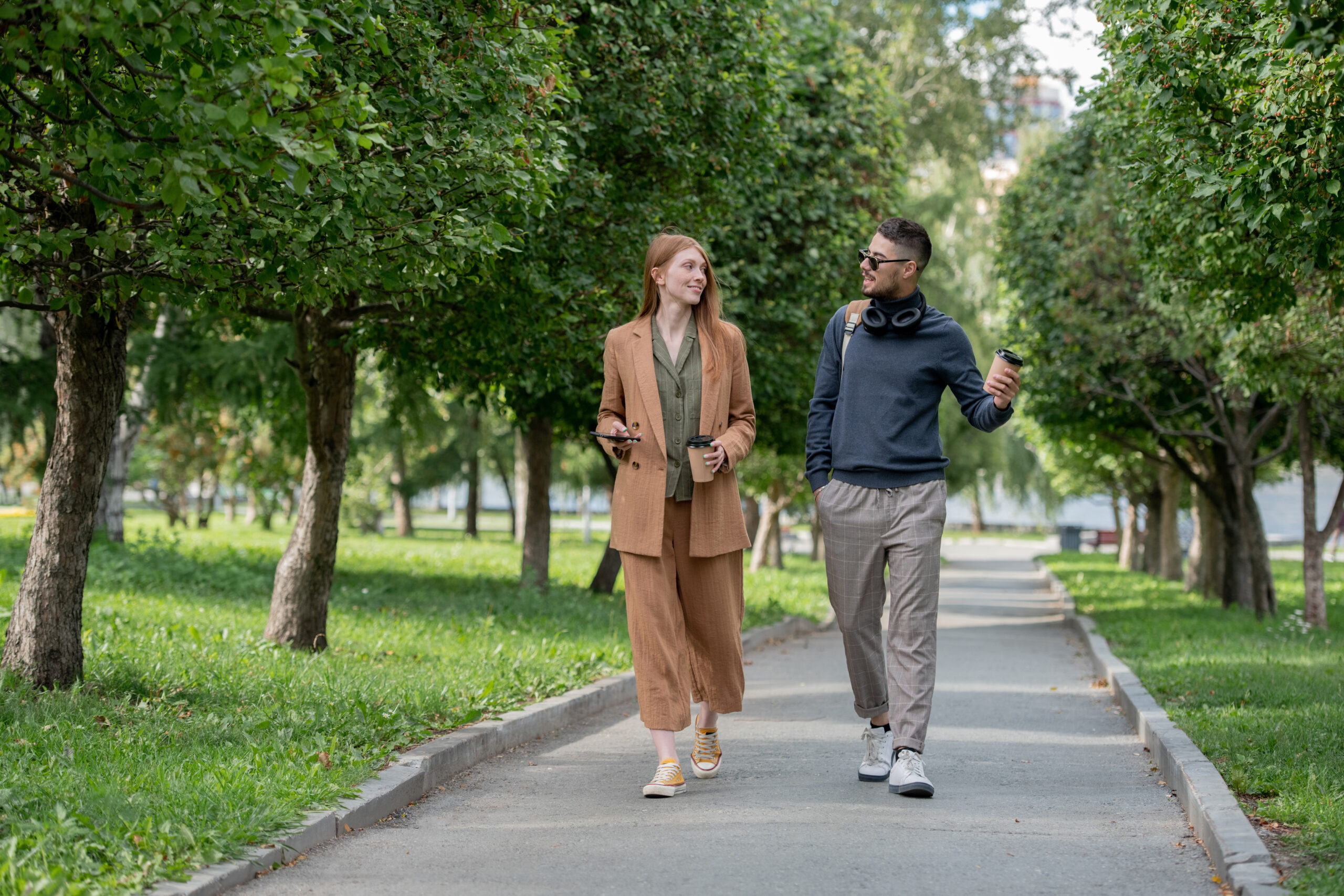 Young man and woman walking and talking on a tree-lined park path